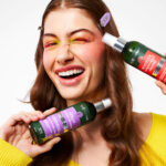 Uśmiechnięta kobieta prezentuje dwa kosmetyki do pielęgnacji włosów w sprayu.